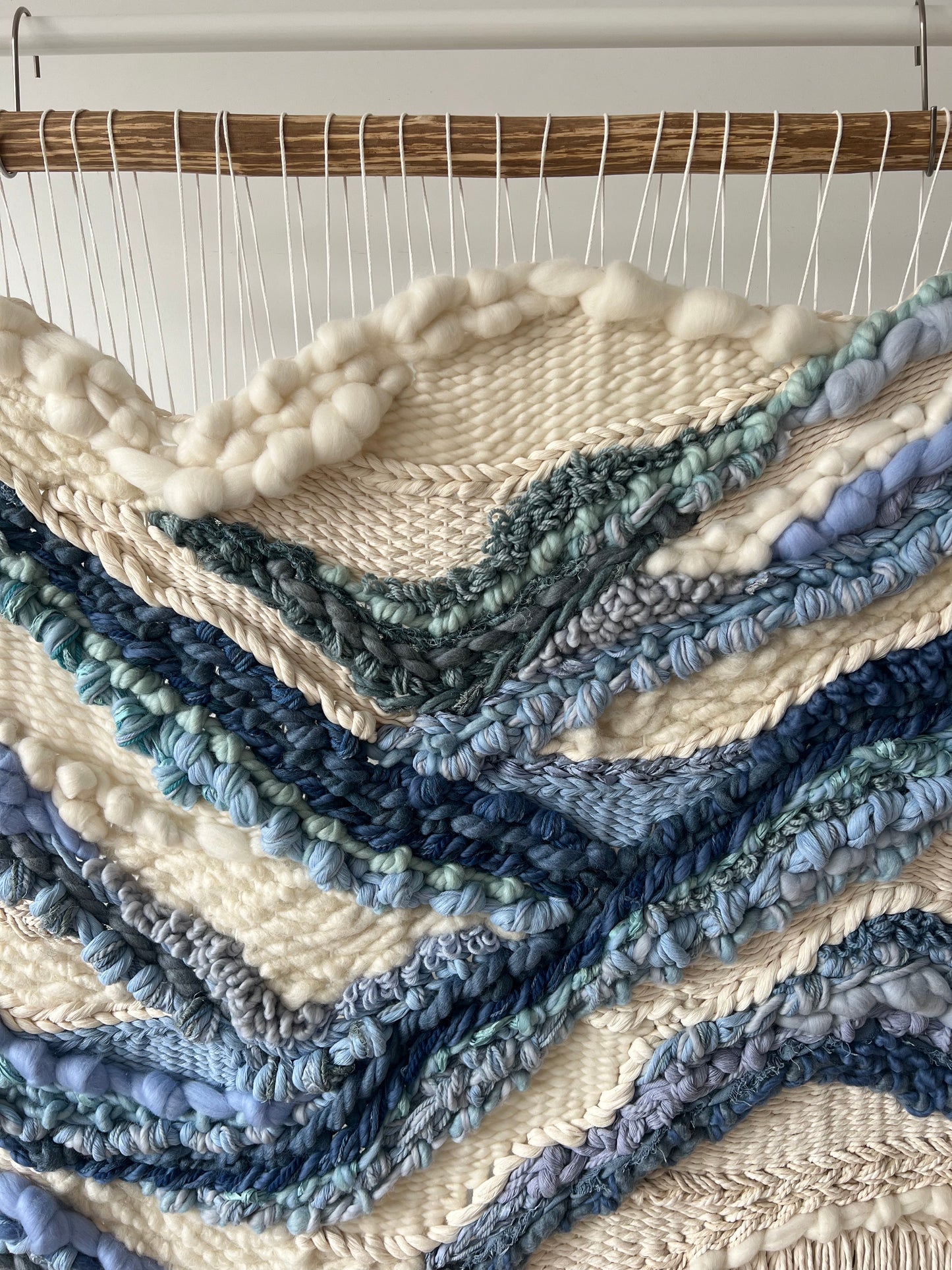 Close-up of abstract blue river pattern on textured cream wool panel