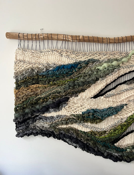 Close-up of woven tapestry showing intricate texture and mixed fibers in cream, moss green, and teal.