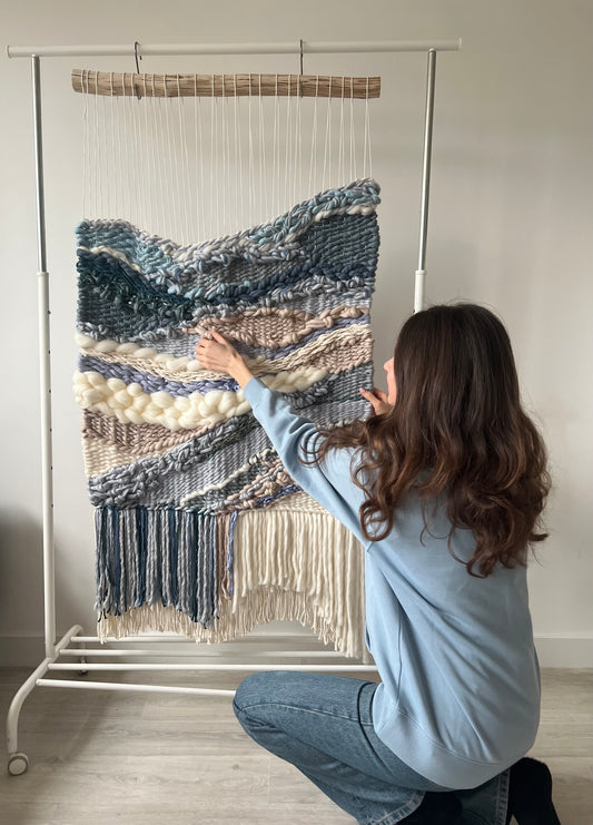 Artist standing next to Ocean Drift handwoven wall tapestry in blue and beige tones