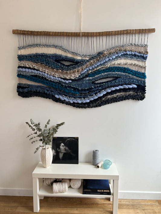Handwoven tapestry 'Breath of the Ocean' with ocean-inspired waves in blue and grey tones, wall decor above console table
