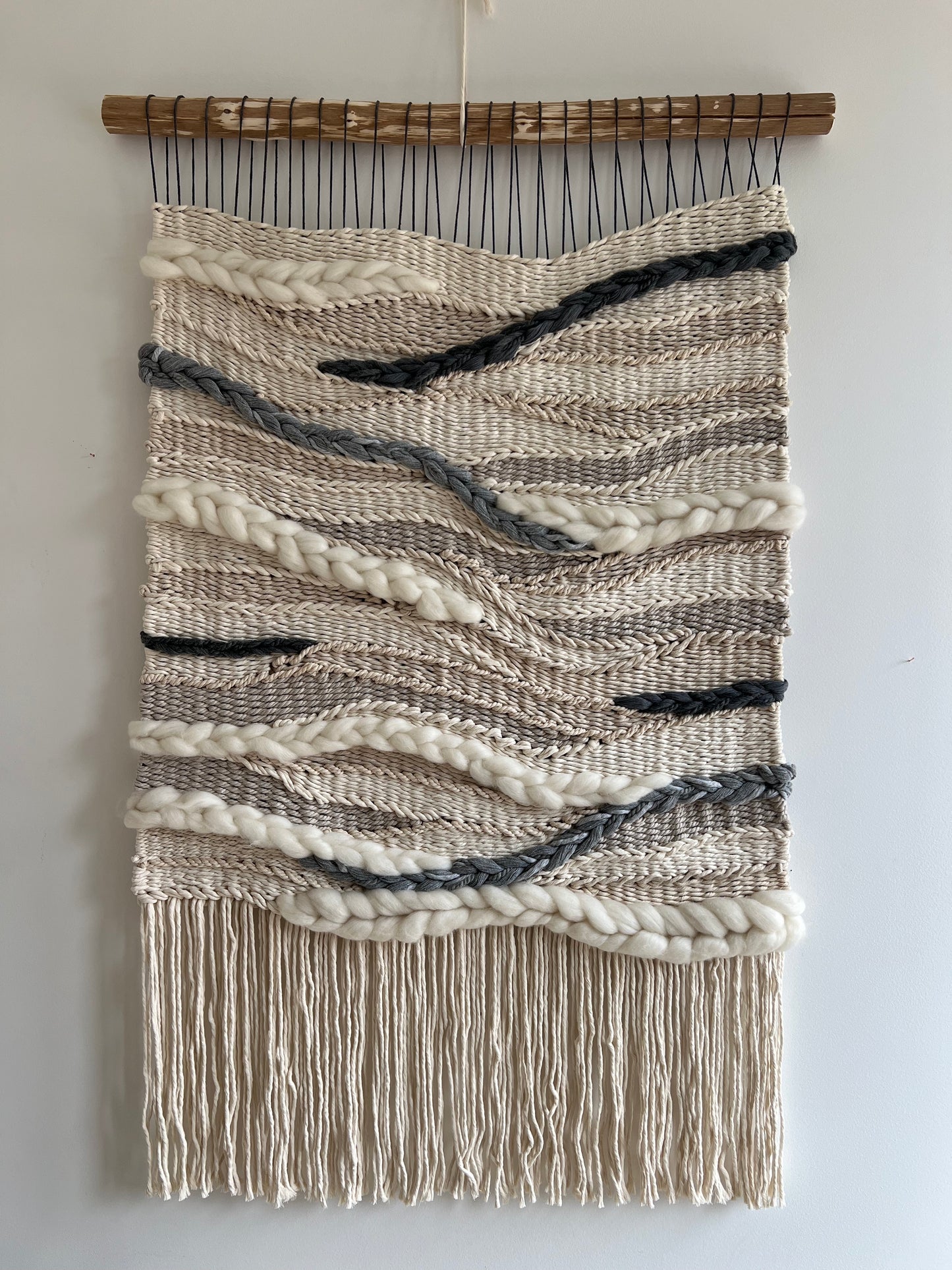 Stone River” wall hanging on a white wall, modern woven art in earthy neutral colors