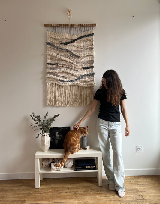 Artist with the “Stone River” woven wall hanging in neutral cream and gray tones