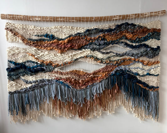 Full view of handwoven textile wall art in terracotta and blue tones featuring flowing forms and balanced composition