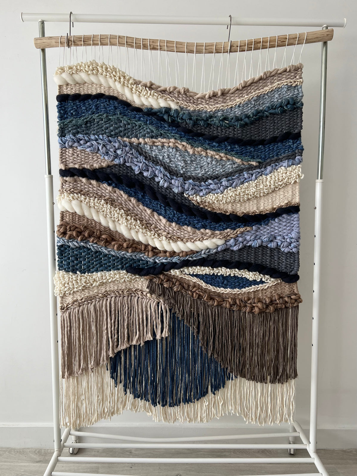 Handwoven wall hanging on wooden display stand, showcasing boho-style woven textures in navy, cream, and brown yarns