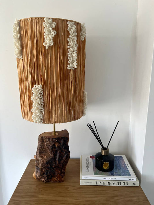 Handmade raffia and ash wood lamp on a wooden table, showing natural wood grain and woven raffia shade.