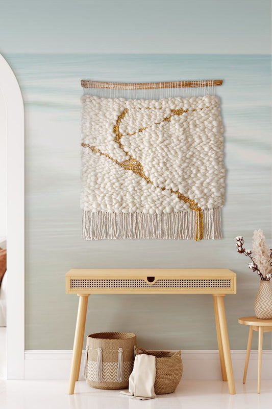 Vertical woven wall hanging in calming tones styled above a console table in a hallway