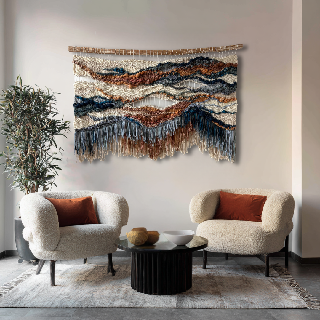 Handwoven fiber art in terracotta and blue tones displayed between two lounge chairs in a cozy meeting space