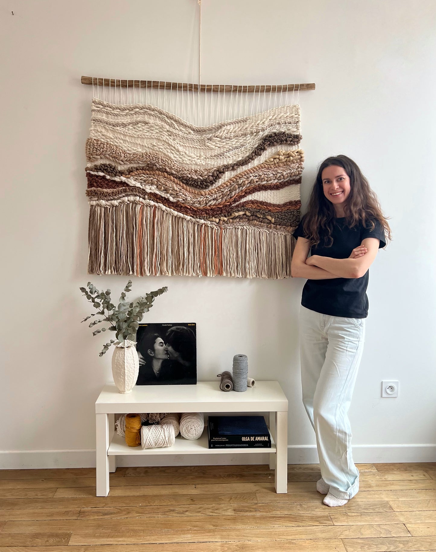 Portrait with the textile wall hanging in earthy tones – photo of the artist standing beside the wool and cotton panel
