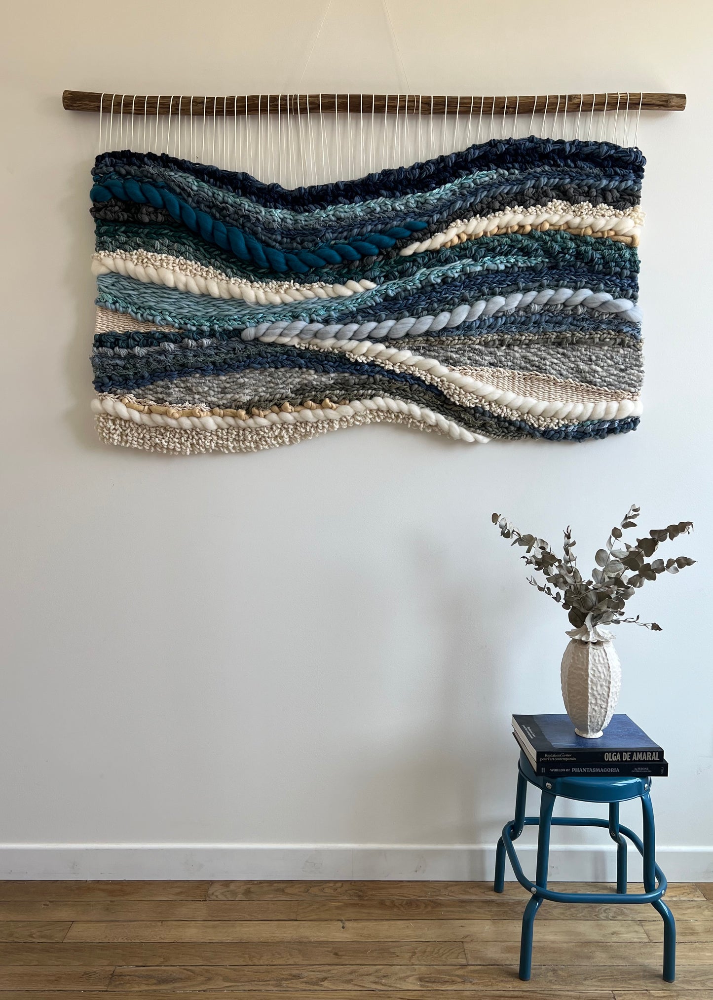 Horizontal wool tapestry in glacier-inspired blue palette hanging on plain wall