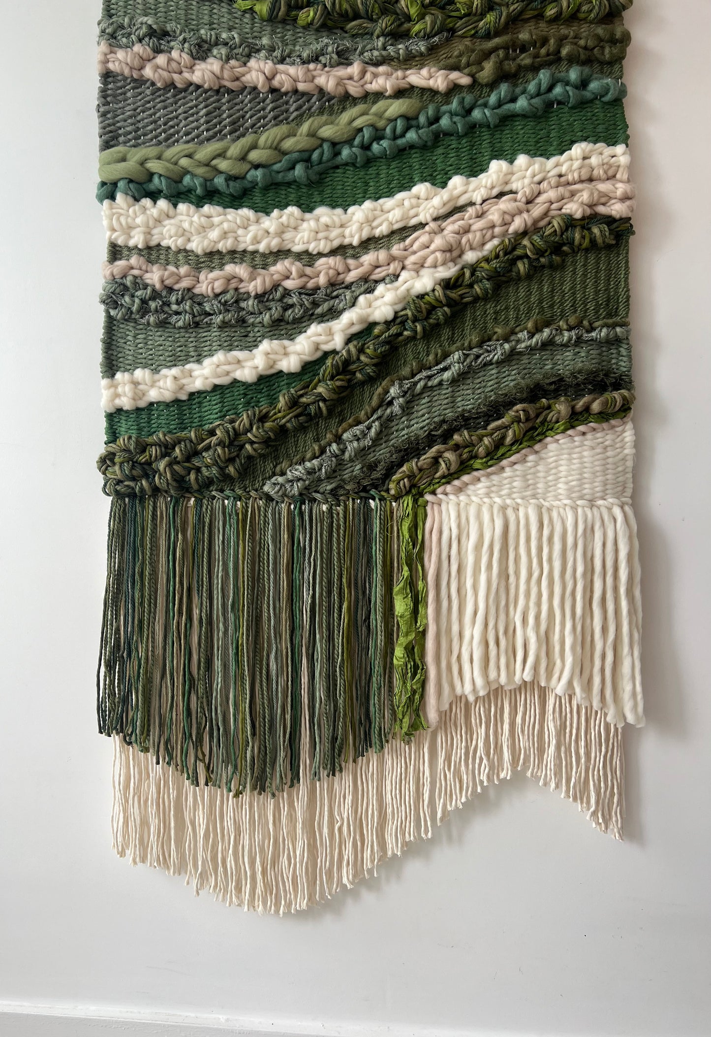 Close-up of the fringe at the bottom of the wool and cotton wall hanging in cream and green