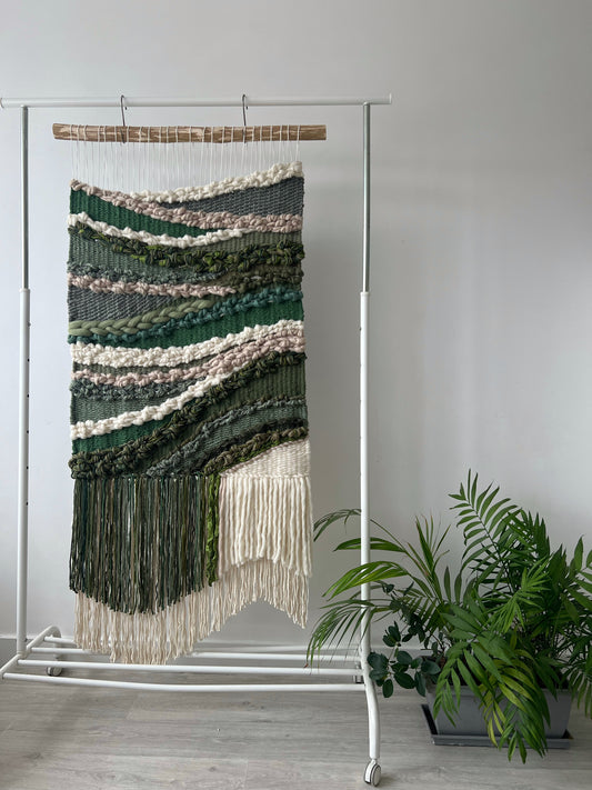 Green wool and cotton wall hanging, displayed beside a potted plant.