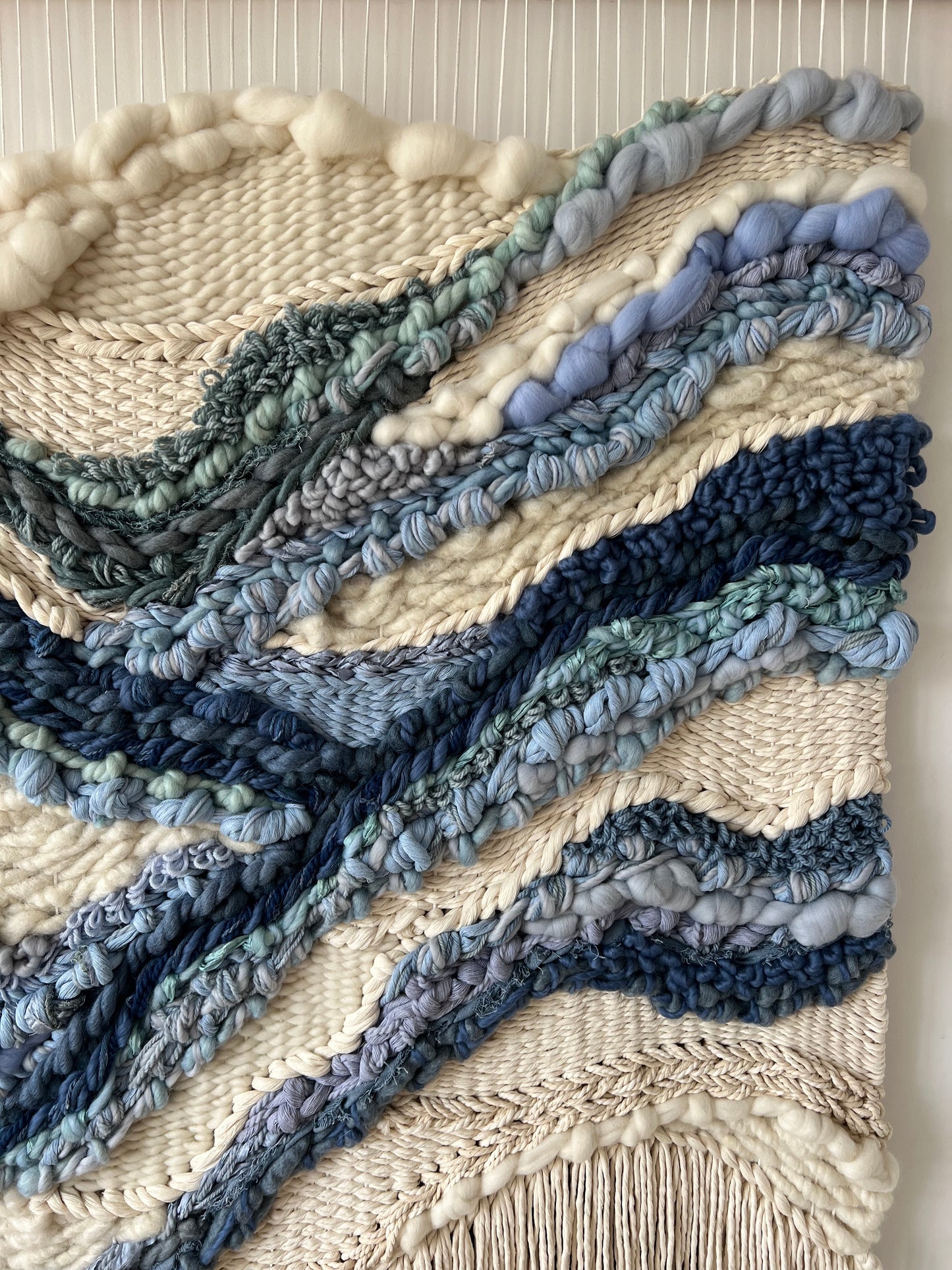Side angle view of vertical cream tapestry with deep blue woven lines