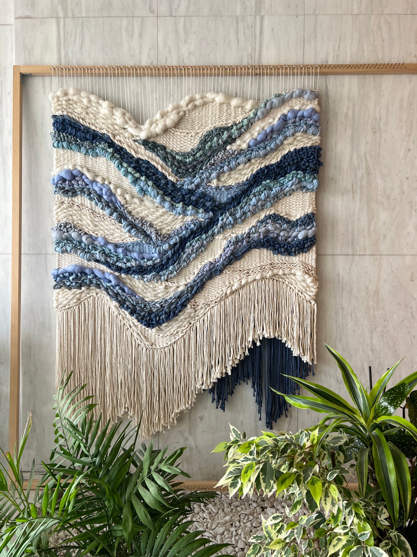 Handwoven tapestry on loom, cream background with blue river-like design