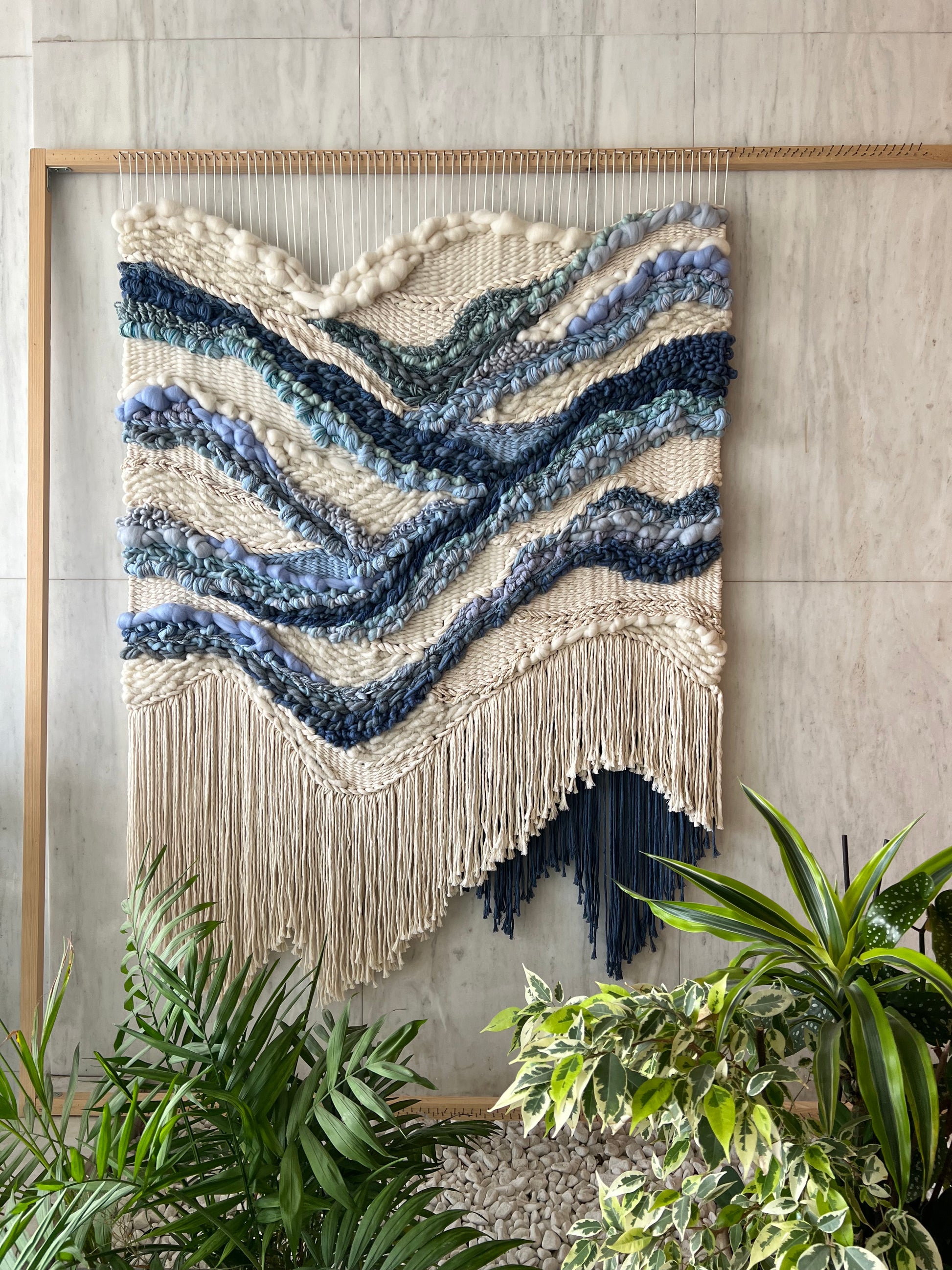 Handwoven tapestry on loom, cream background with blue river-like design