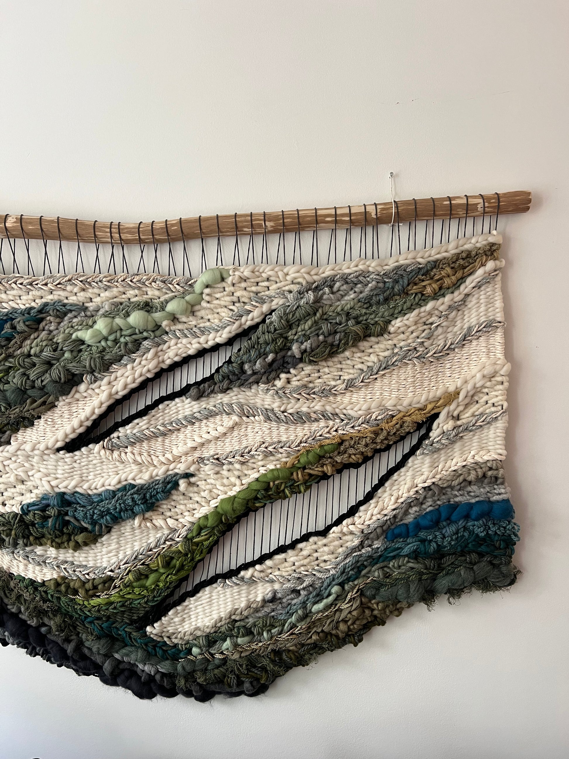 Textured section of woven wall art featuring bold fibers in green, gray, and blue hues with natural flow.