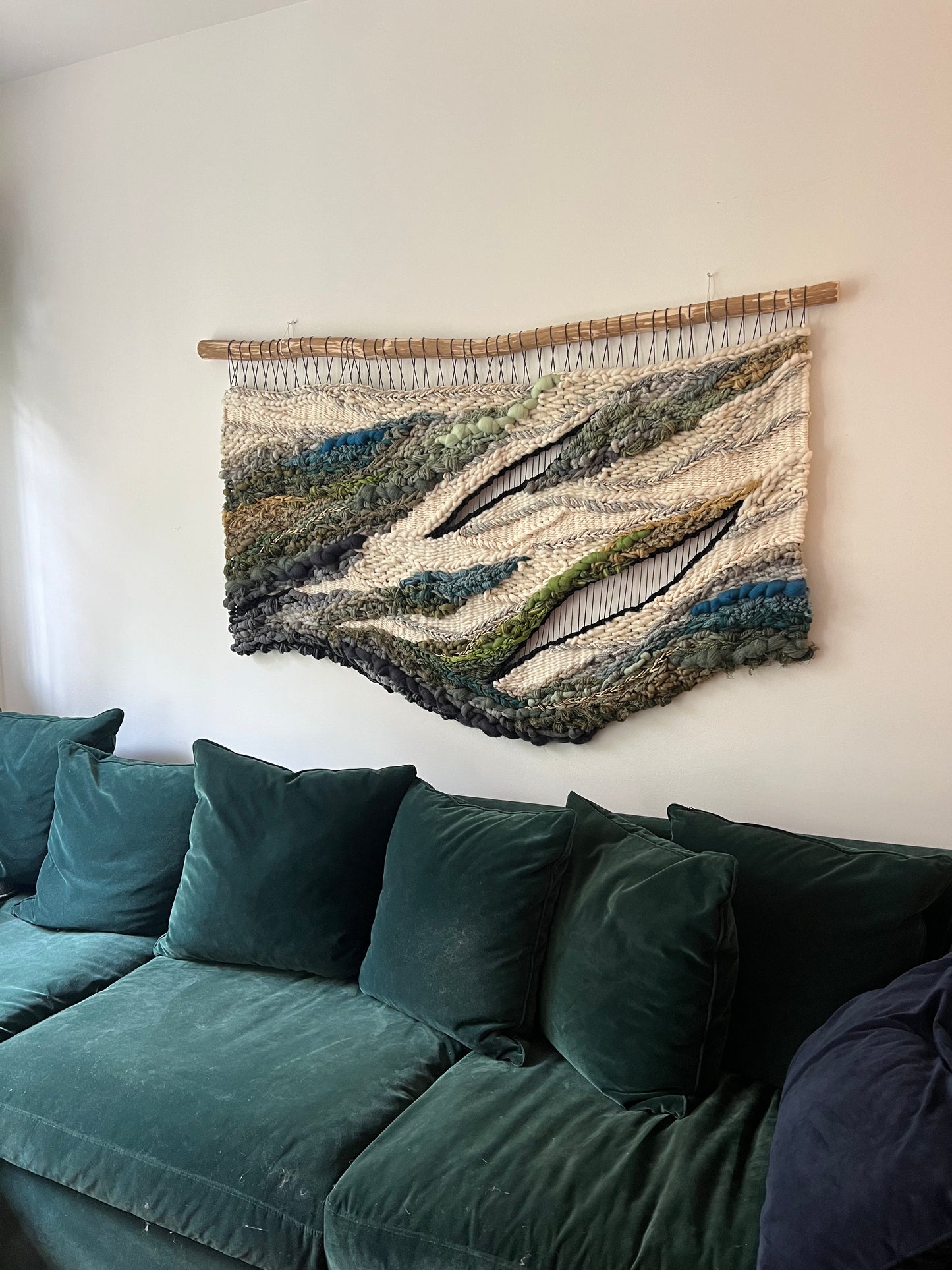 Side view of handmade woven wall art with textured layers of wool and fiber in natural greens, blues, and neutrals