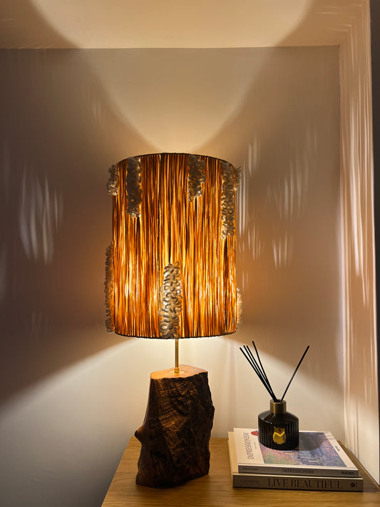 Handmade raffia lamp illuminated at night, creating warm ambient light and textured shadows.
