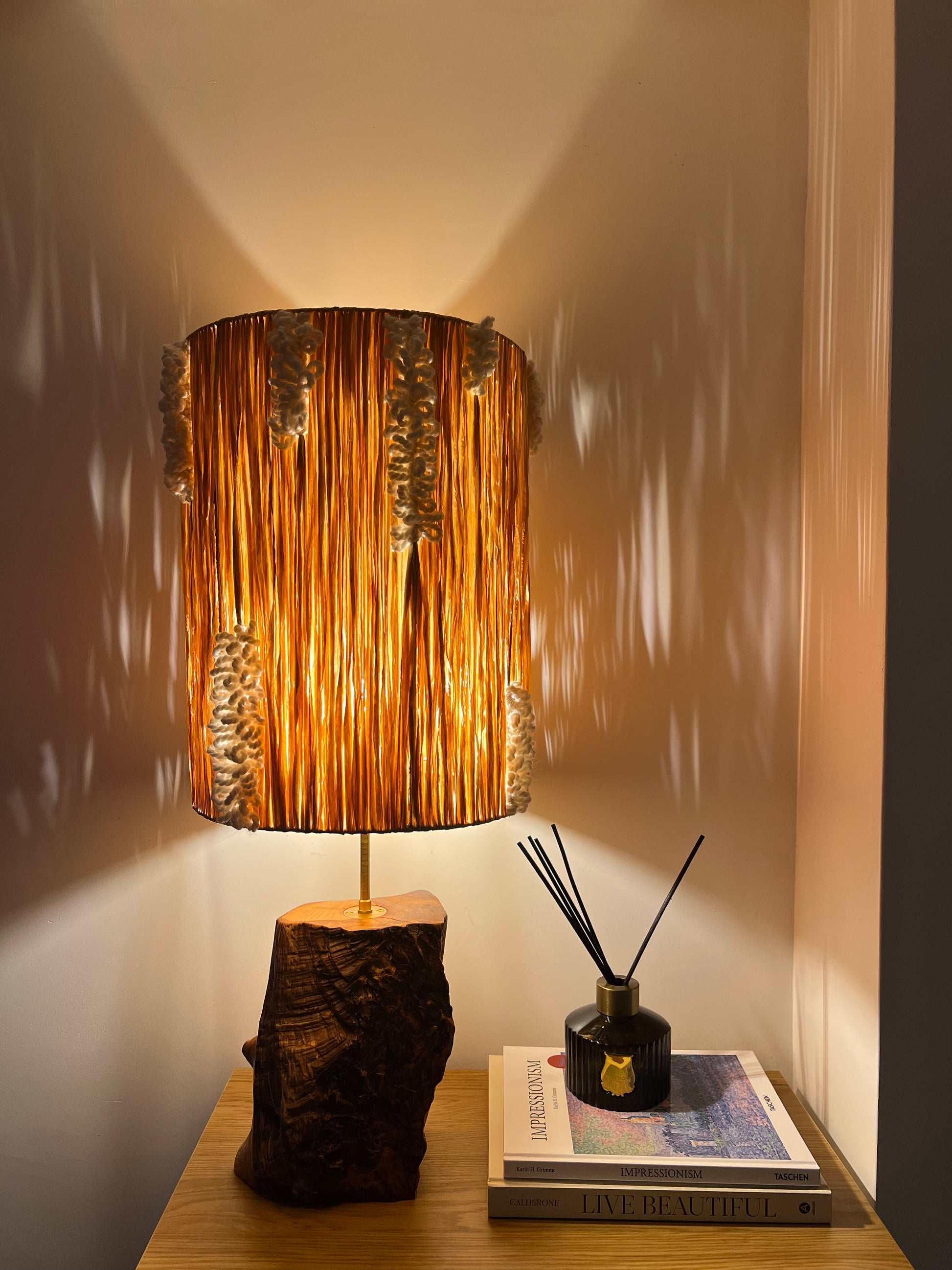 Raffia and ash wood lamp glowing in the dark, casting decorative shadows on the wall.
