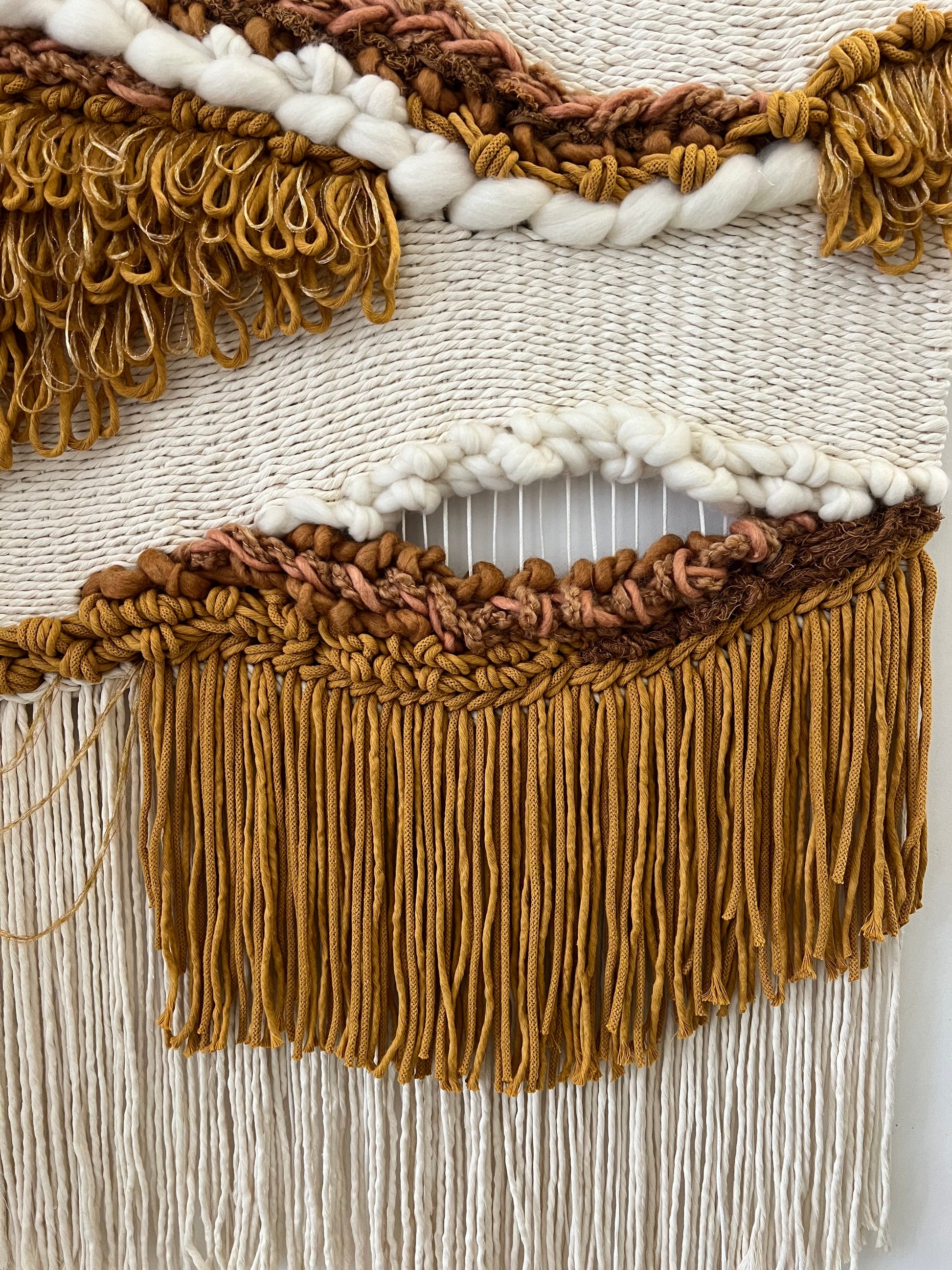 Detailed view of handwoven fringe and mustard yarn accents on wall hanging