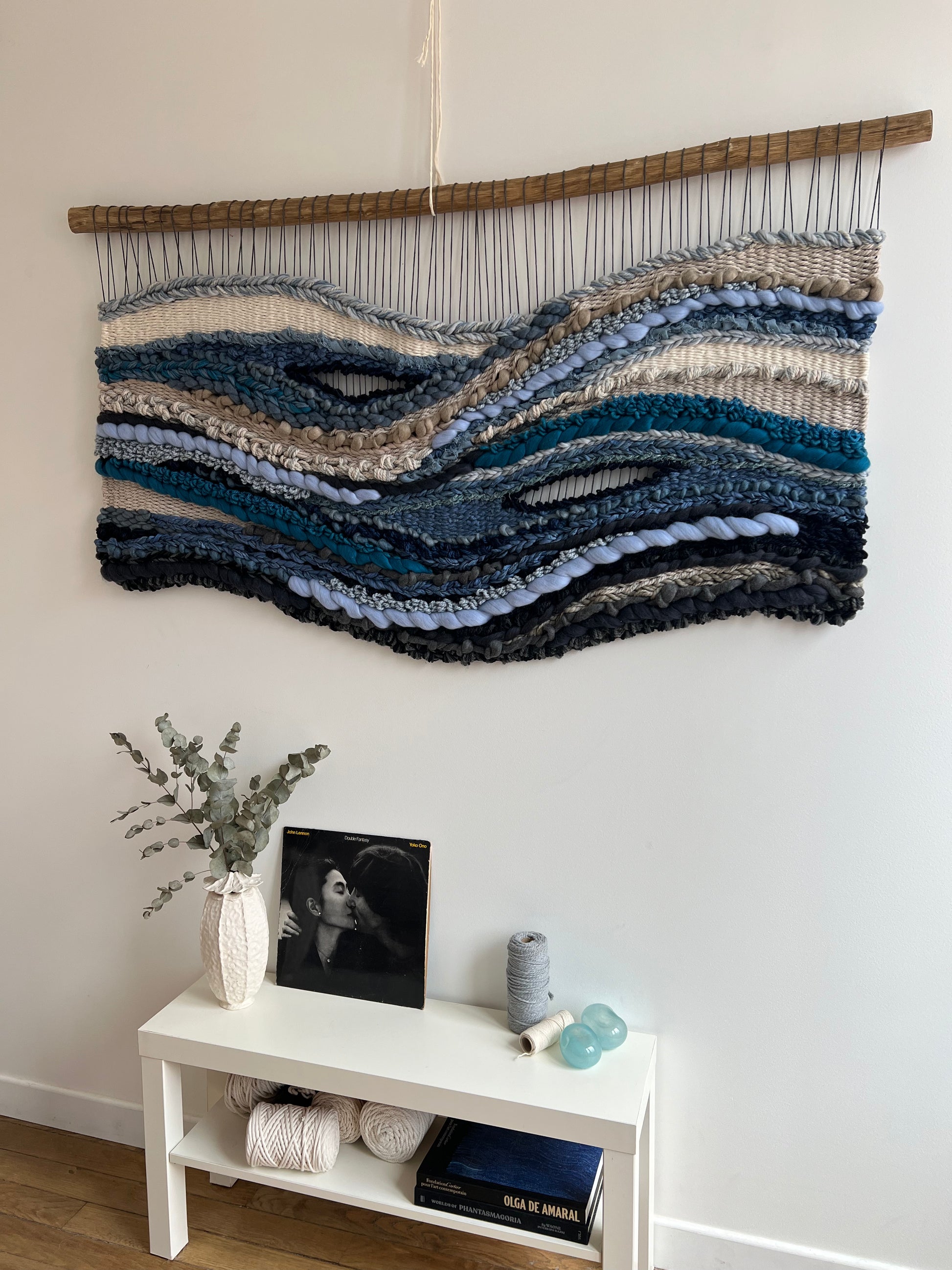 Angled side shot of handwoven ocean-inspired tapestry in soft blue, grey and cream colors