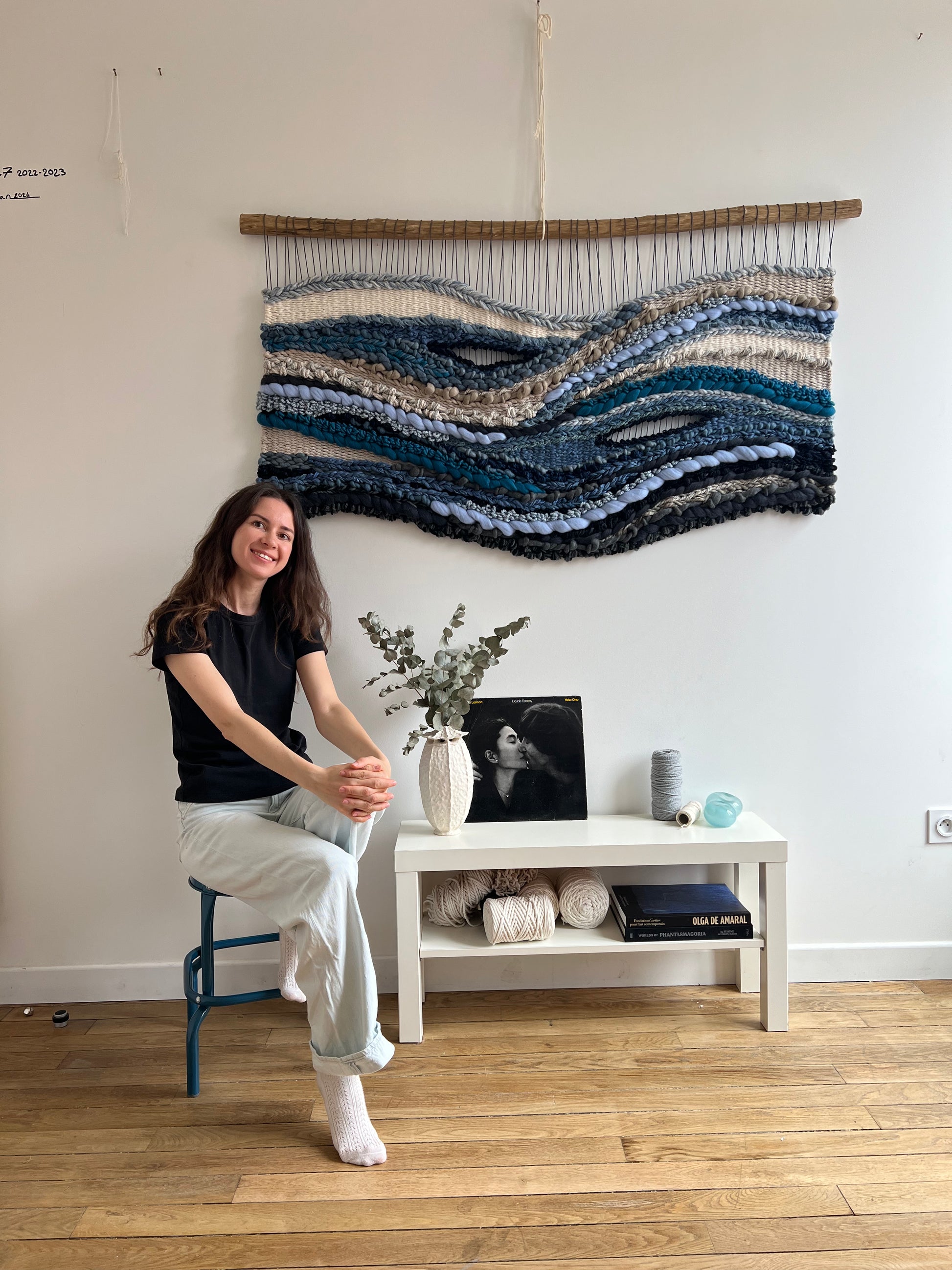 Fiber artist with large woven wall hanging 'Breath of the Ocean' in blue, grey and cream tones, handmade fiber art tapestry.