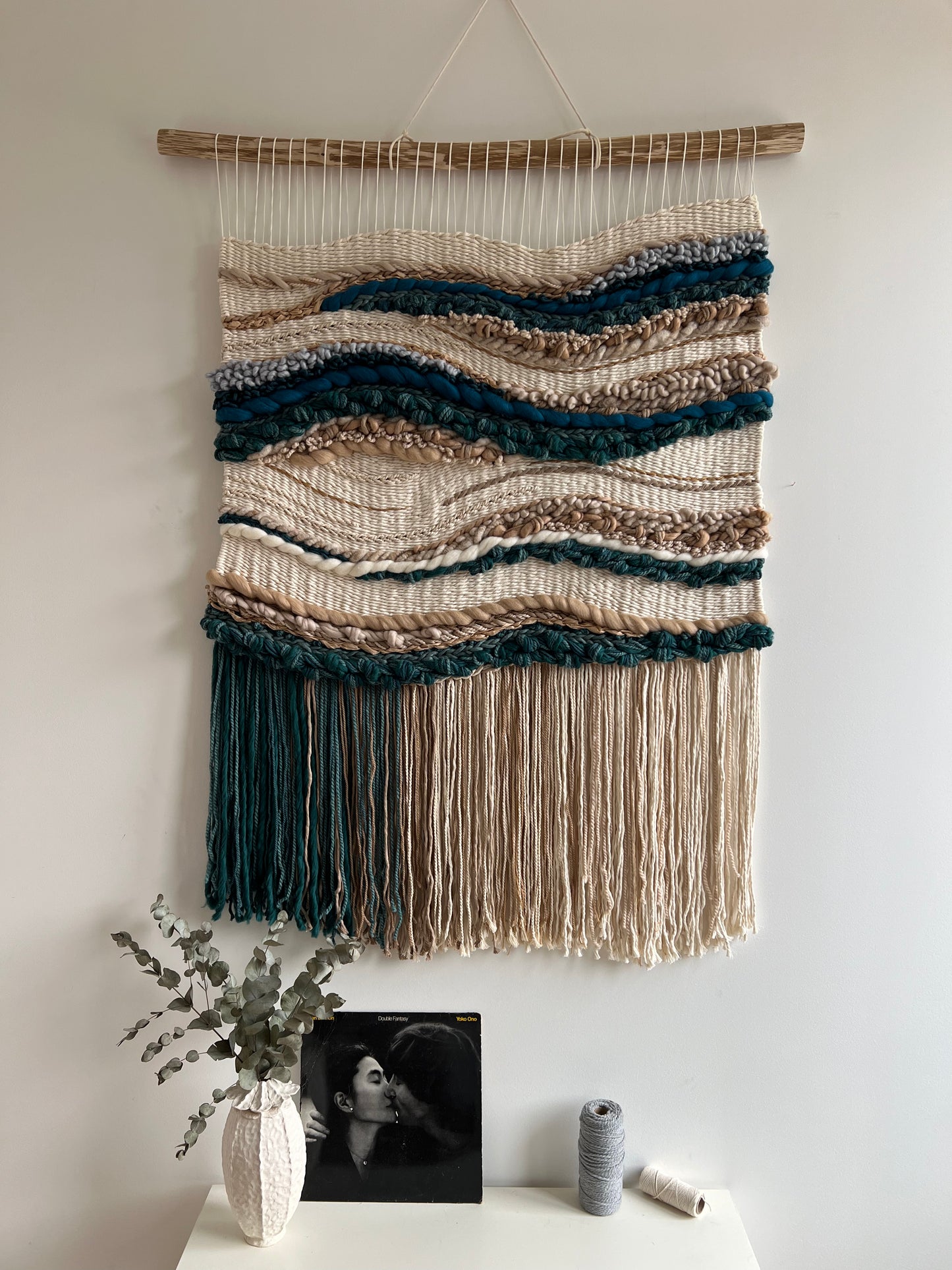 Blue and beige fiber art wall hanging styled above console table with decor accents