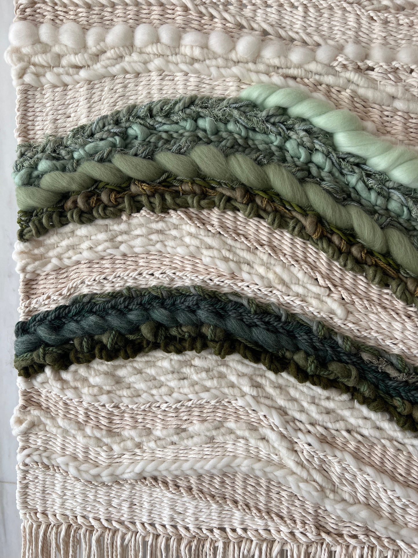 Detail of handwoven wall art with textured cream fibers and multiple shades of green yarn