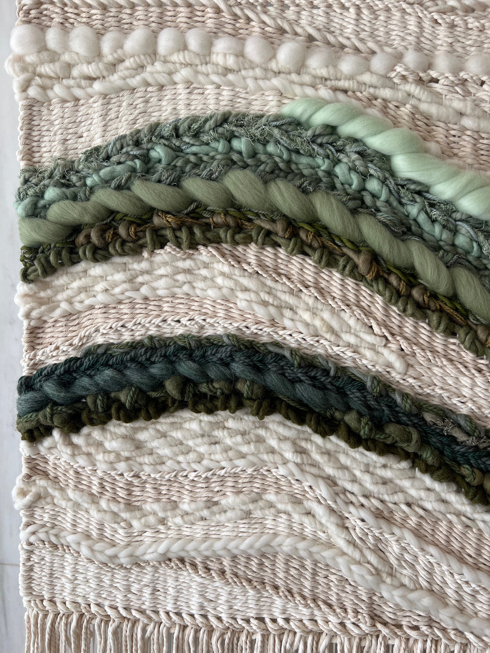 Detail of handwoven wall art with textured cream fibers and multiple shades of green yarn
