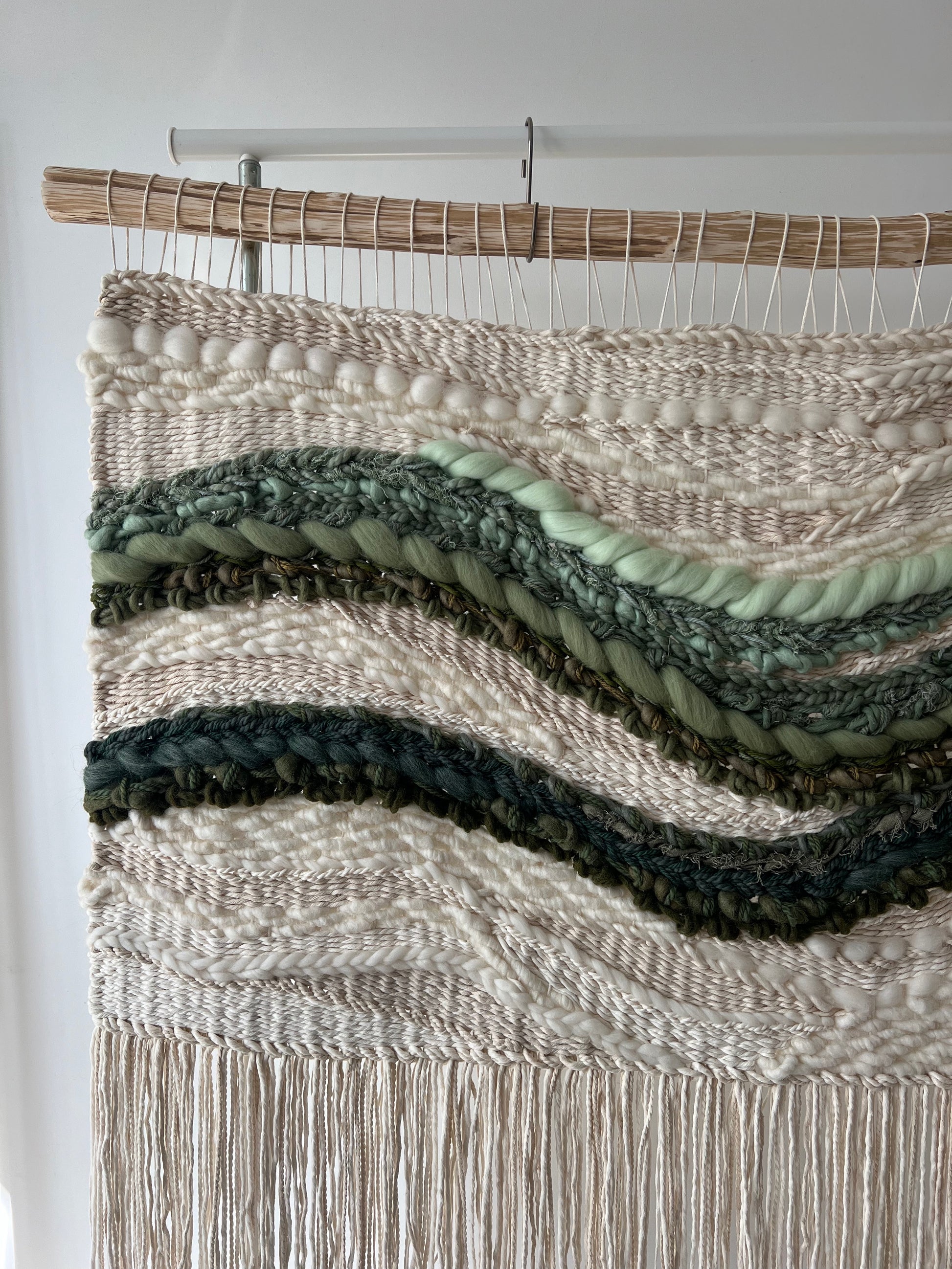 Artistic close-up of square woven tapestry with natural fibers, green wave patterns, and cream background.