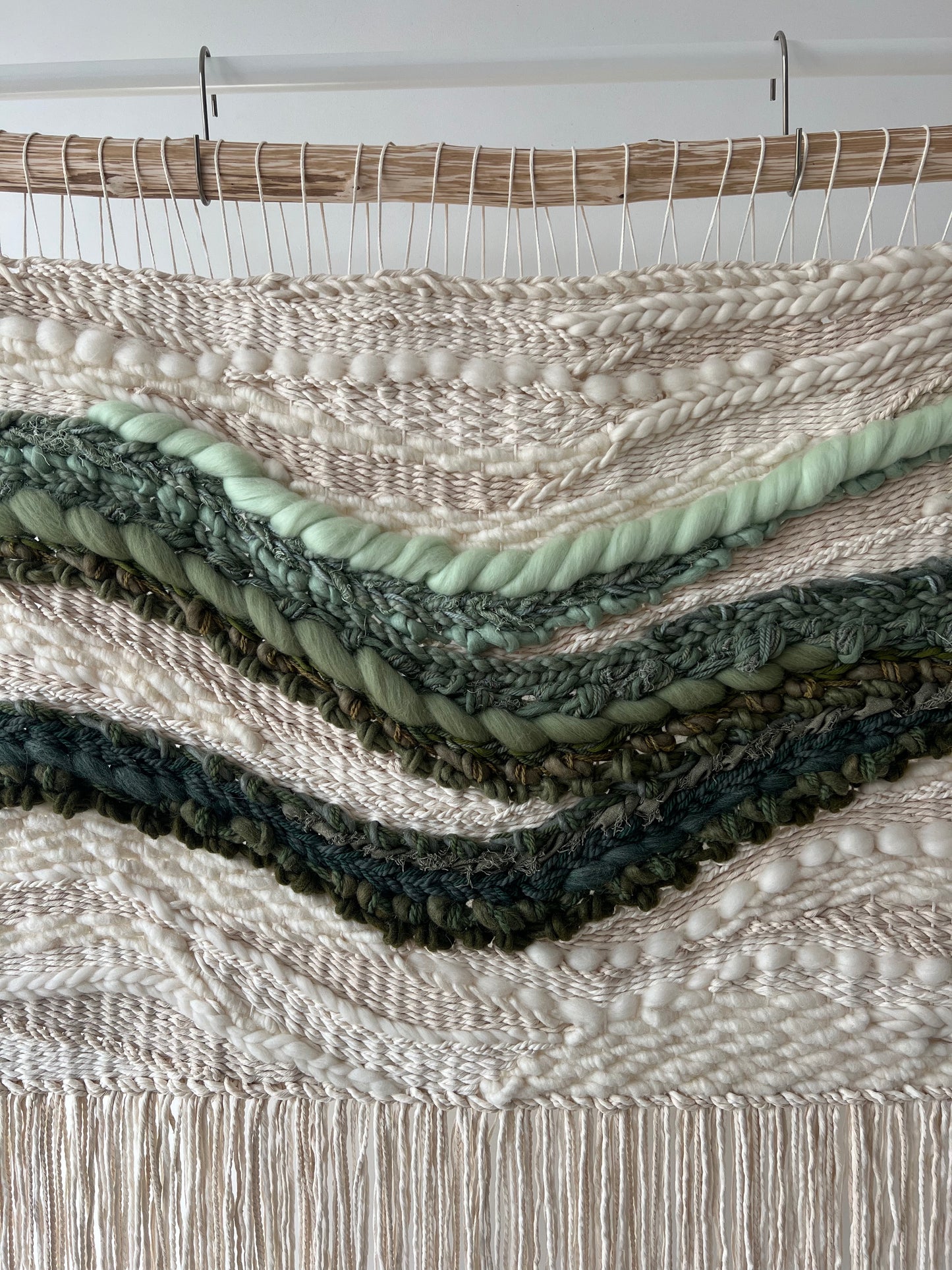 Close-up of woven tapestry showing layered green waves on cream textured base with organic flow