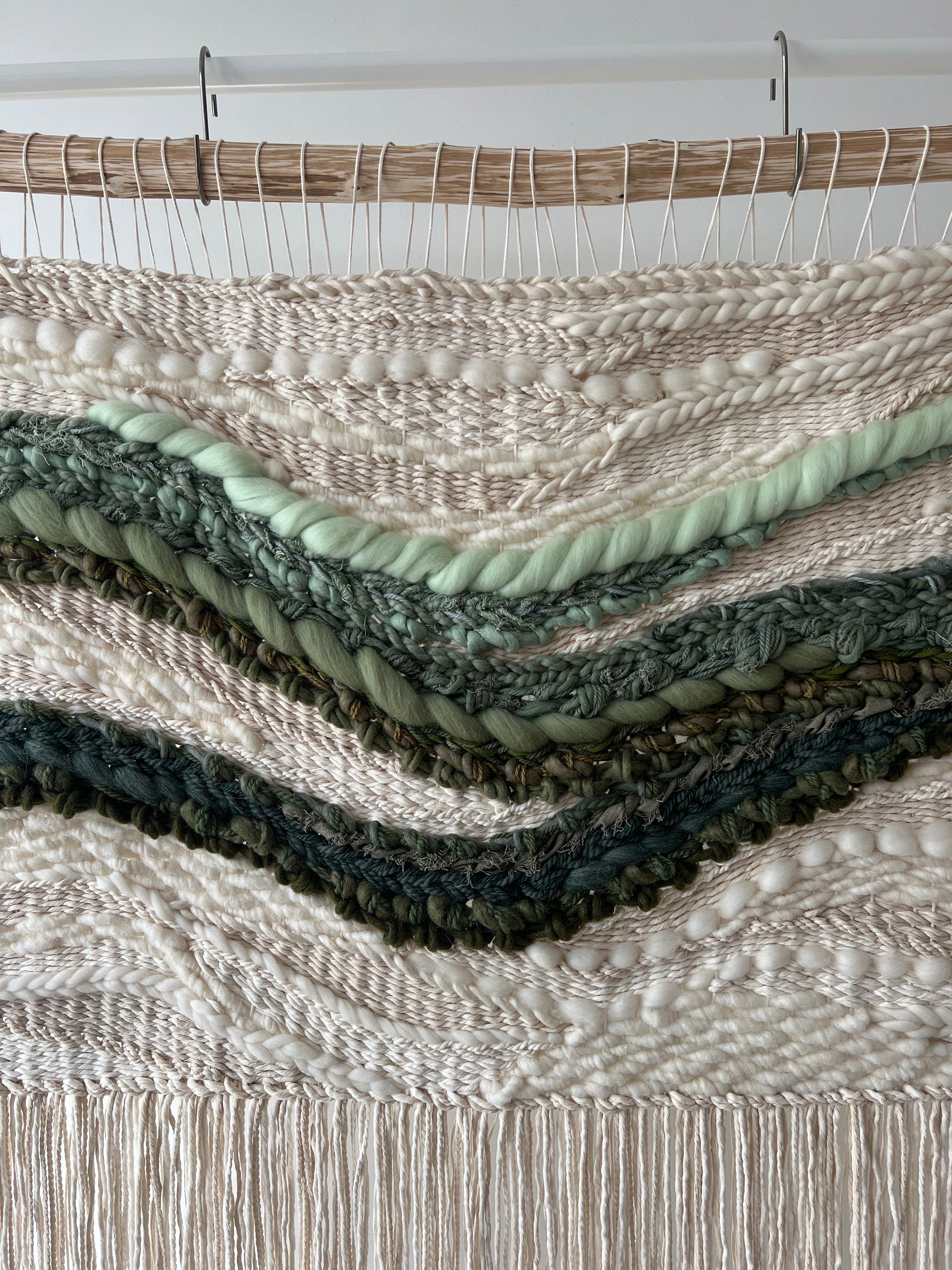 Close-up of woven tapestry showing layered green waves on cream textured base with organic flow