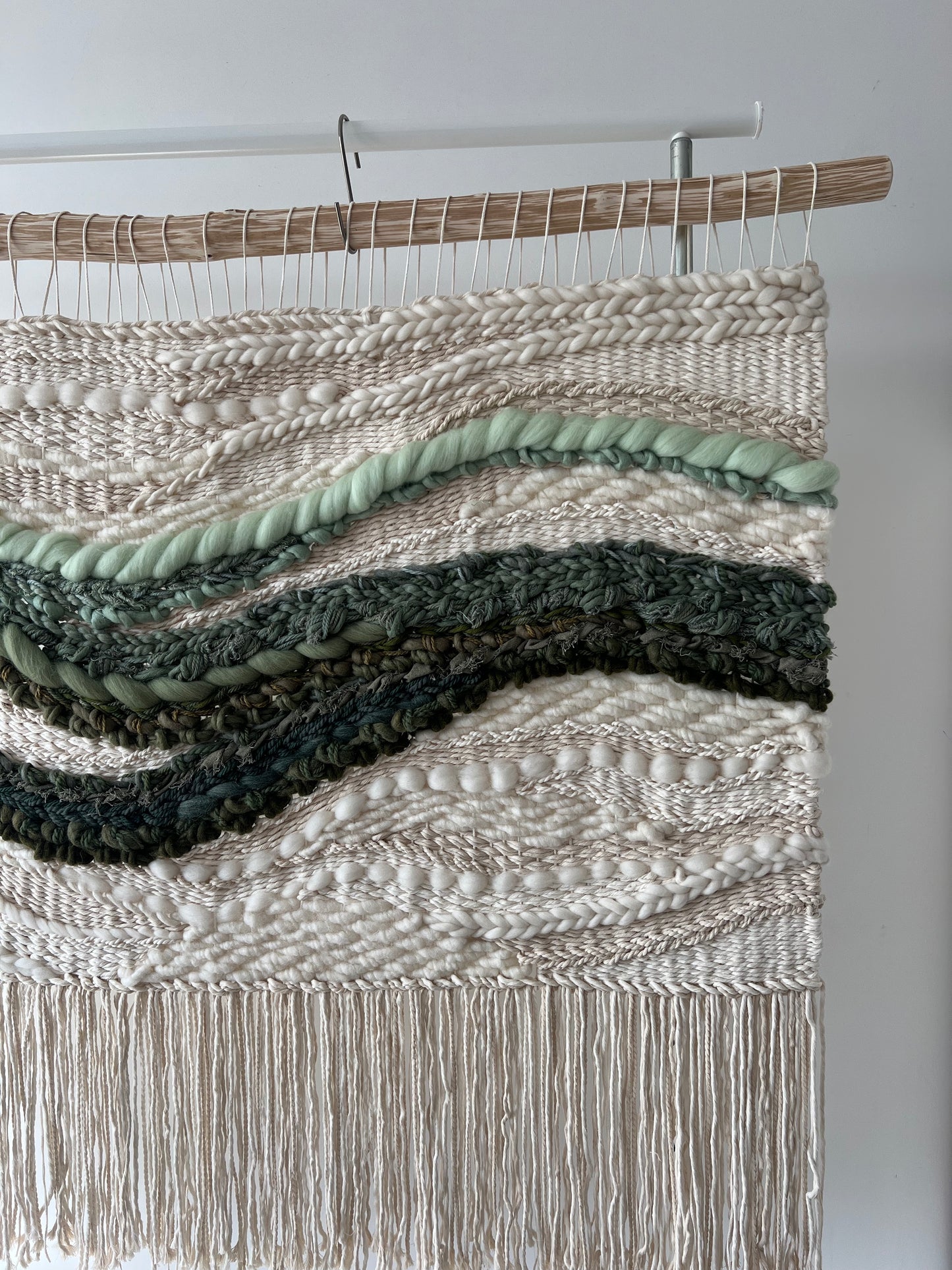 Side details of handmade woven wall hanging with cream base and green wave design