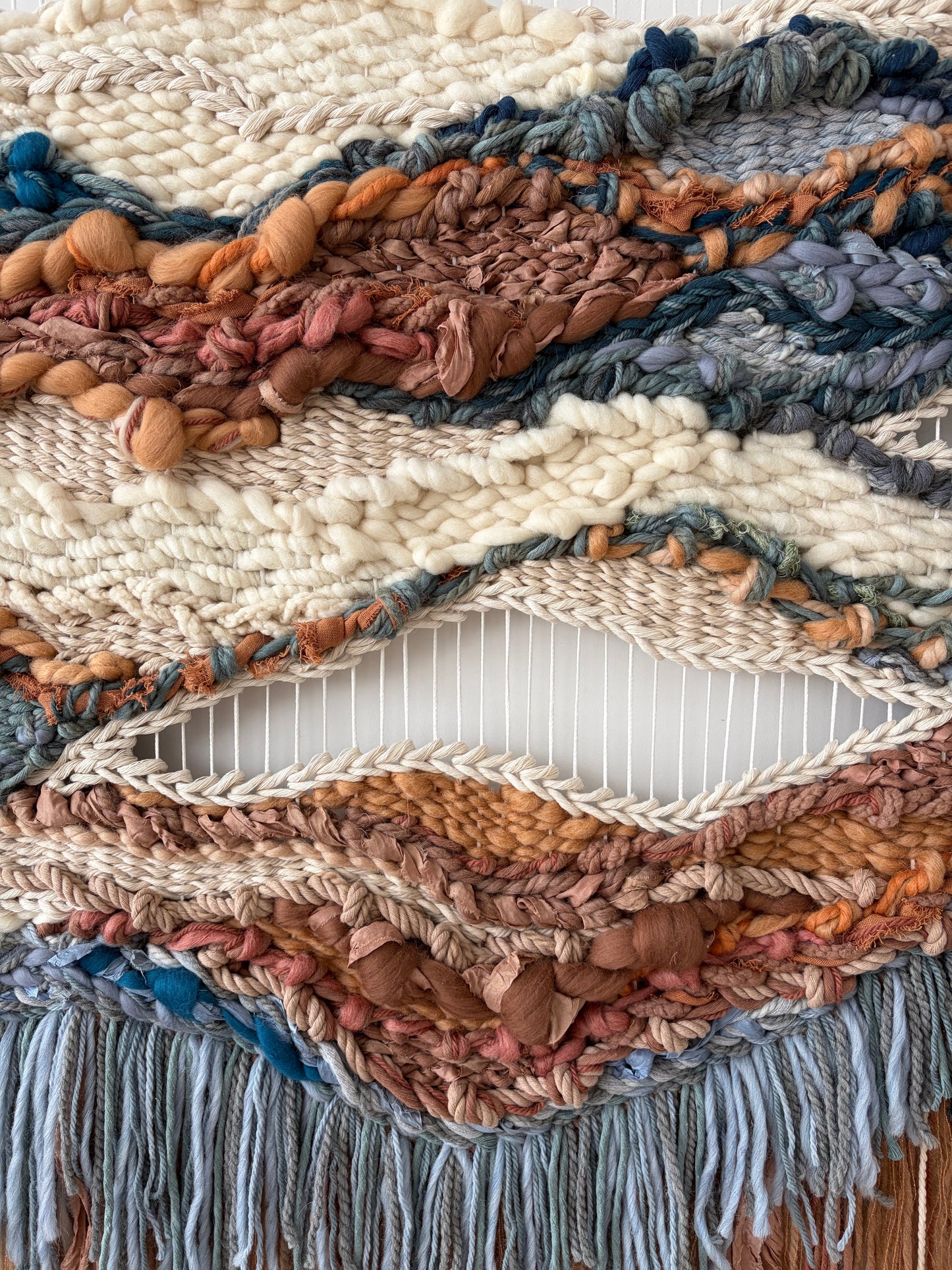 Close-up of textured weaving with mixed fiber density and flowing terracotta and blue threads.