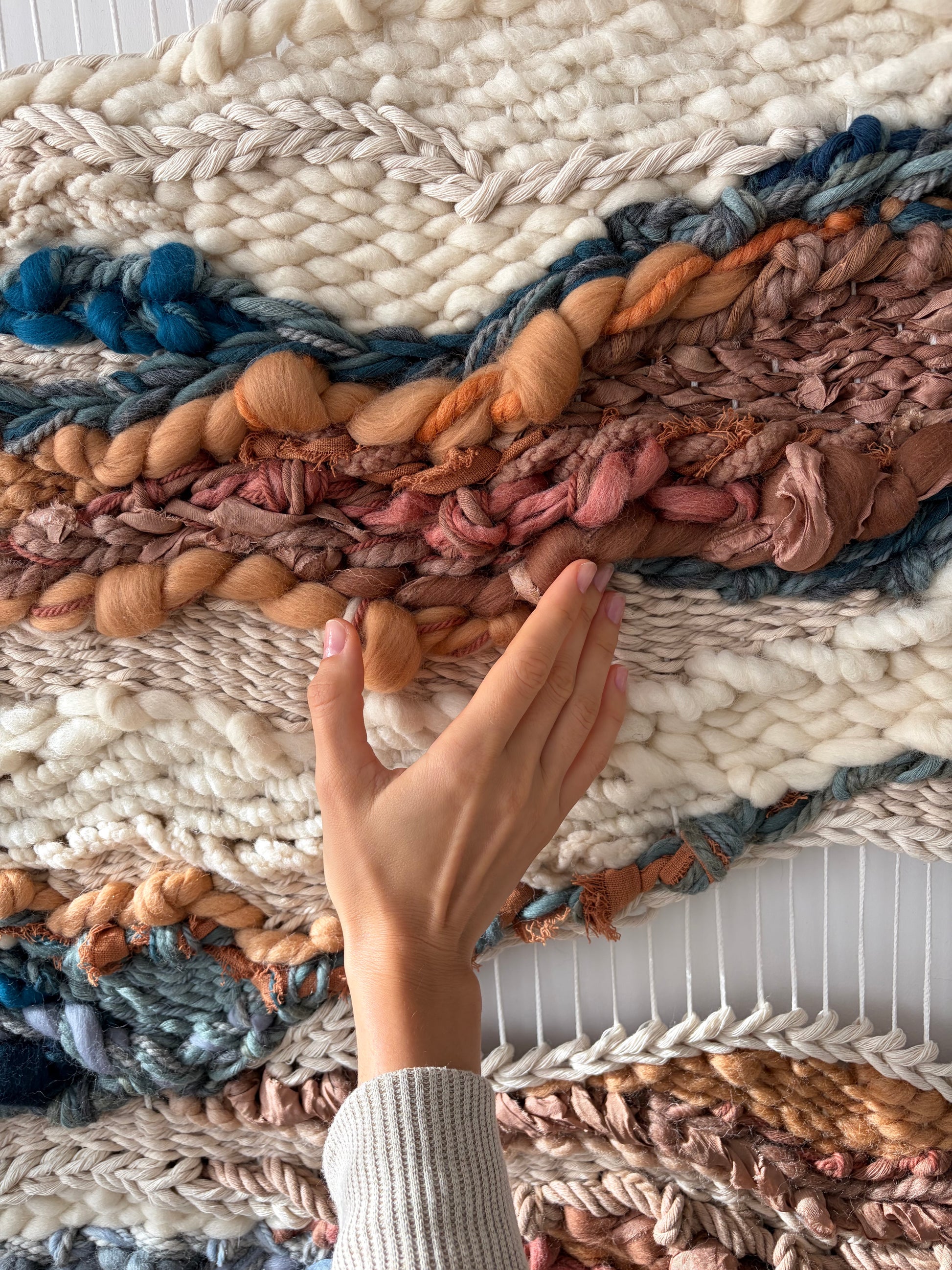 Close-up detail of handwoven textile art showing dimensional weaving and layered fiber textures in terracotta and blue tones