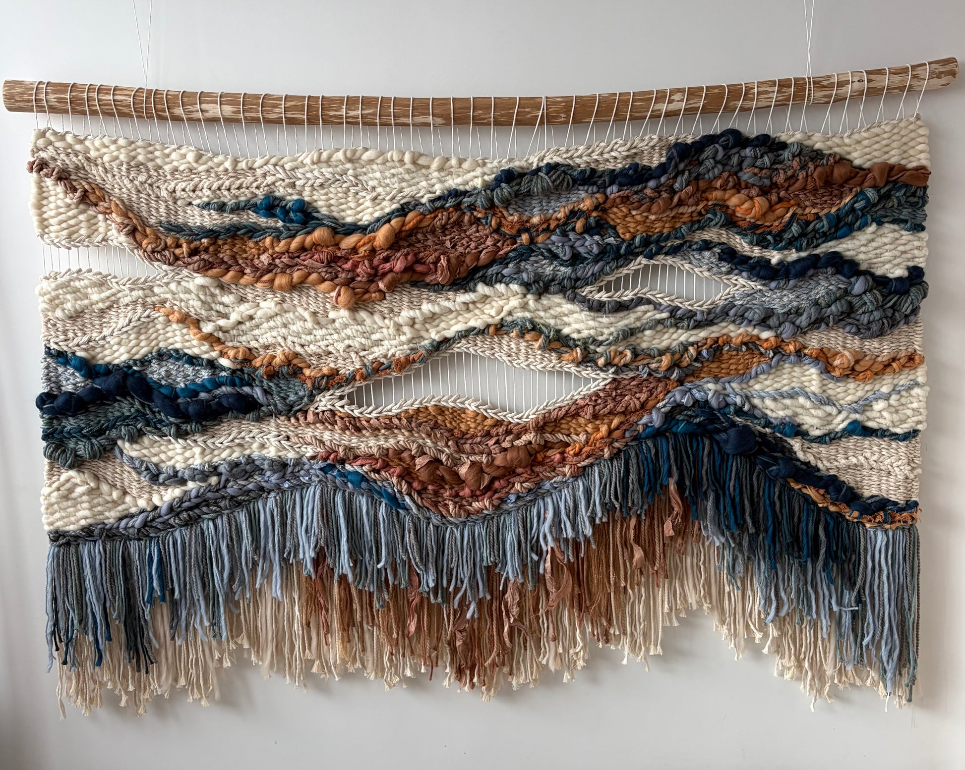 Full view of handwoven textile wall art in terracotta and blue tones featuring flowing forms and balanced composition