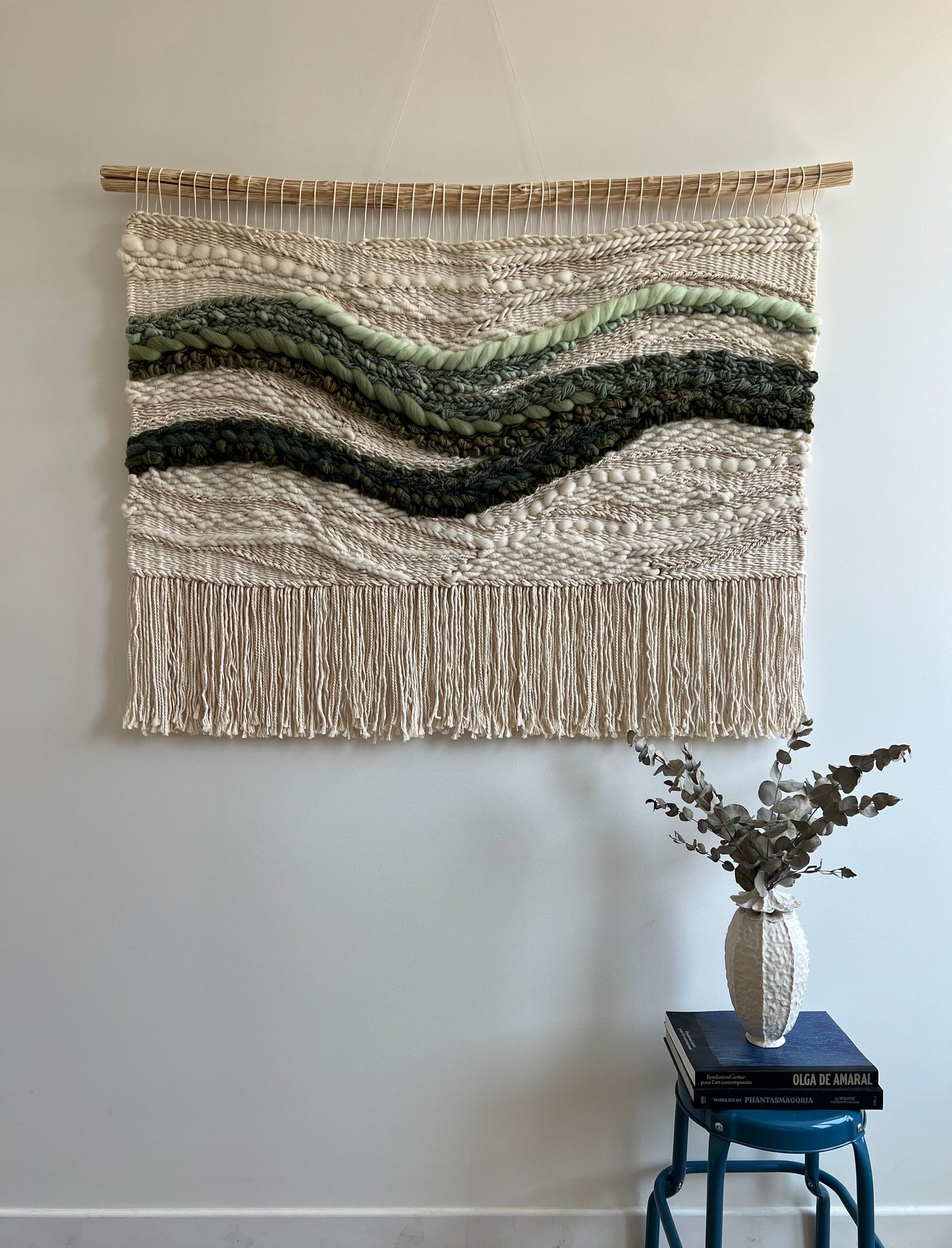 Large square woven tapestry with cream background and layered green wave design, handwoven fiber wall art